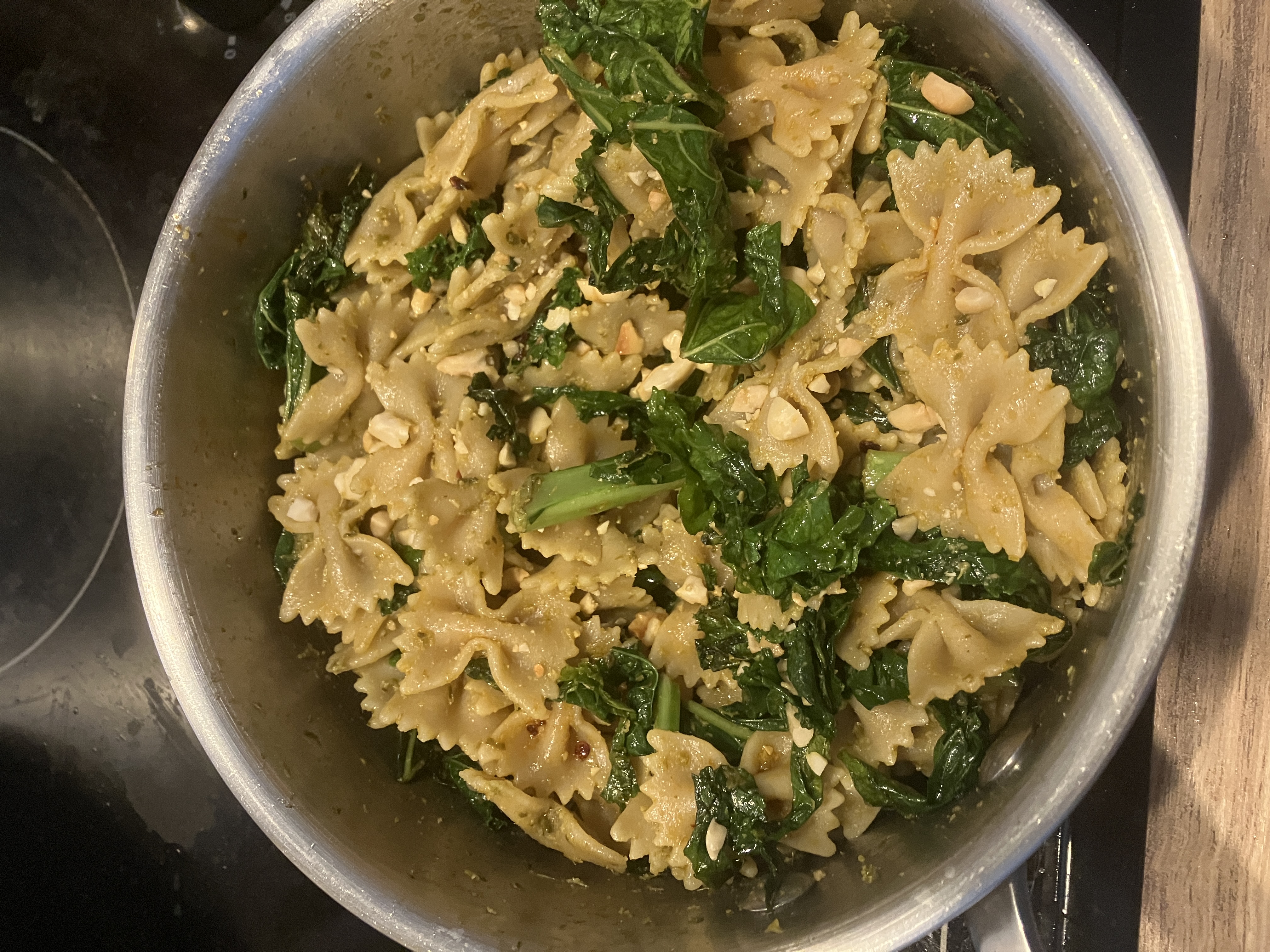 farfalle pasta, with cooked kale leaves, green pesto, chilli flakes and crushed peanuts in a saucepan farfalle pasta, with cooked kale leaves, green pesto, chilli flakes and crushed peanuts in a saucepan