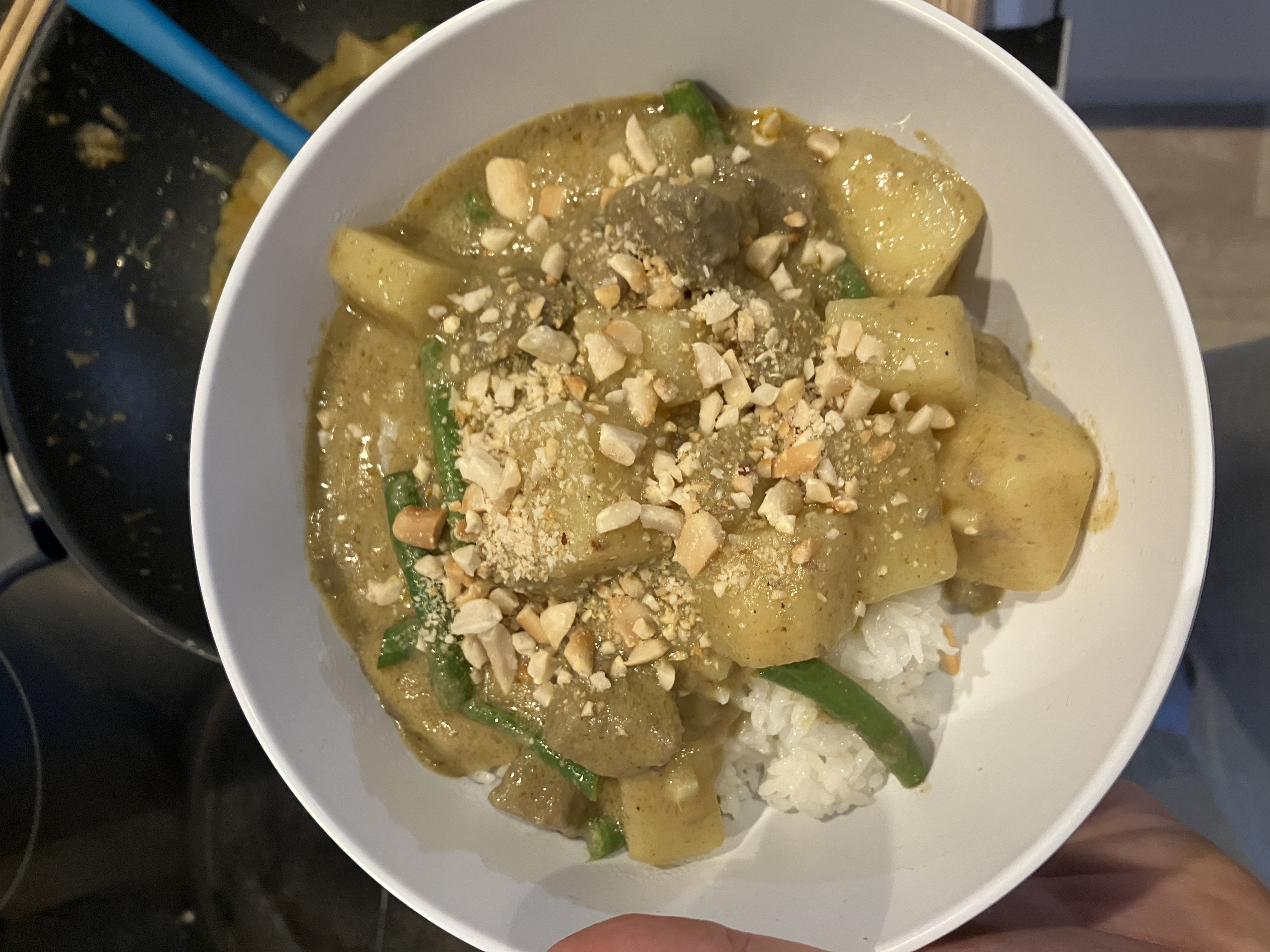a bowl of yellow curry with potatoes, beef and green beans over rice. there are crushed peanuts sprinkled on top a bowl of yellow curry with potatoes, beef and green beans over rice. there are crushed peanuts sprinkled on top