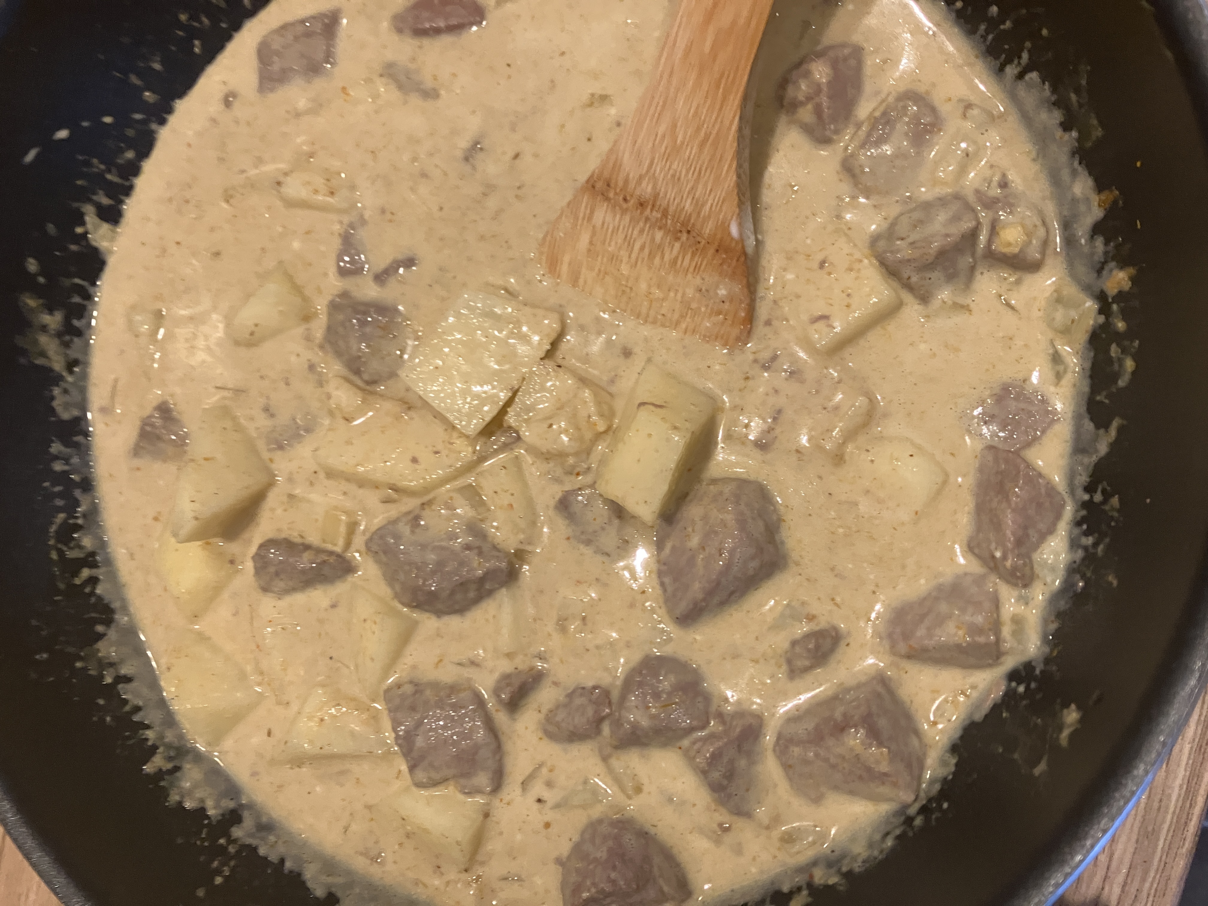 potatoes, beef and green beans in a pale-coloured curry in a wok potatoes, beef and green beans in a pale-coloured curry in a wok